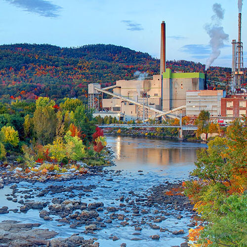 An image of a factory next to a forest and river